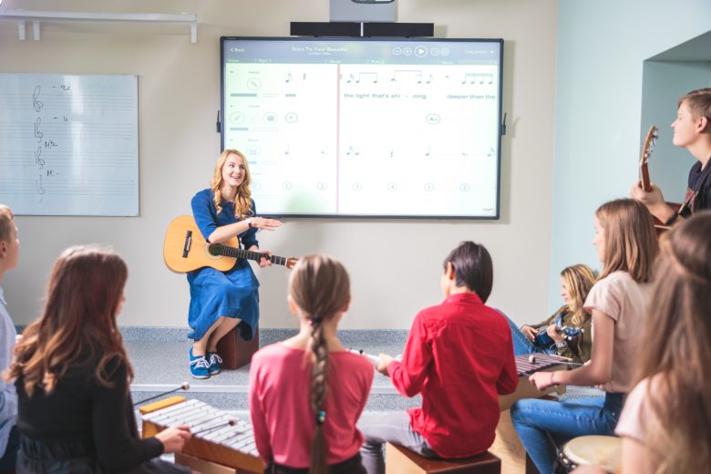 Music teacher guiding children in a music lesson using a digital board